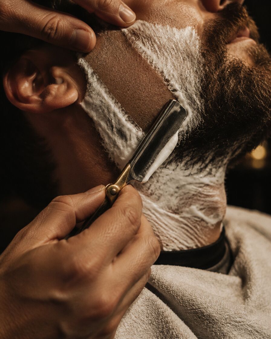 A barber shaving a lathered cheek with a straight razor