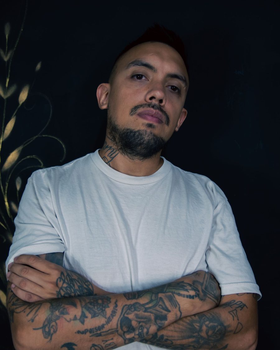 Dario, a tattooed artist in a white T-shirt, standing with his arms crossed