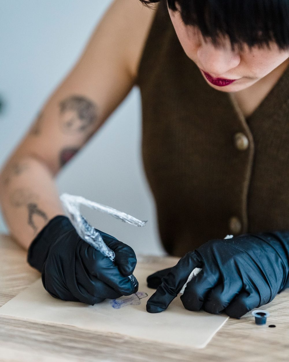 A tattoo artist in black gloves tracing a design onto stencil paper at a bright desk