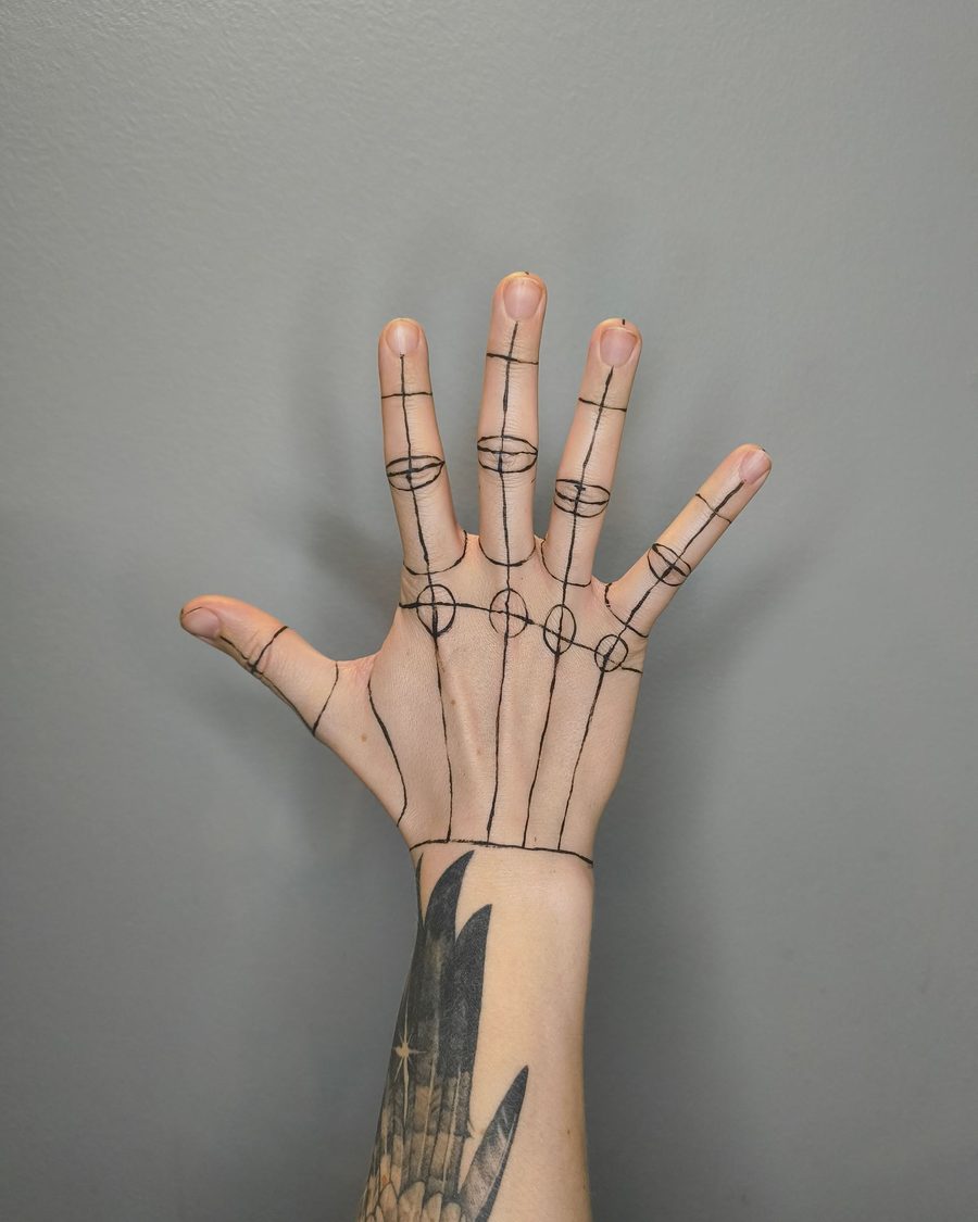 A fine-line skeleton hand drawn over the bones of a real hand, against a grey wall