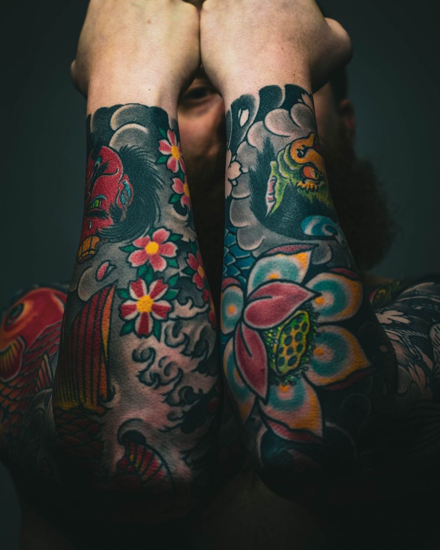 Two forearms with bright traditional flowers and koi in red, teal and yellow