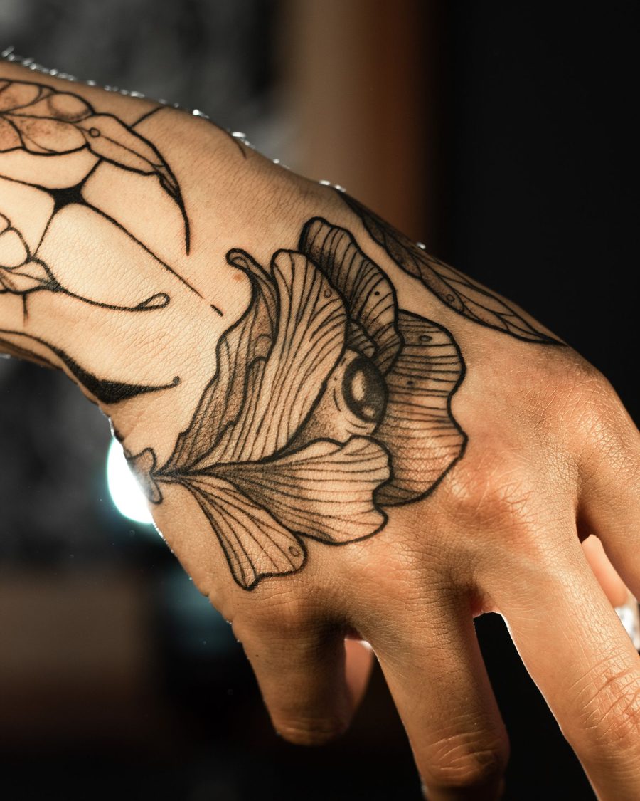 A black linework moth and flower wrapping the back of a hand