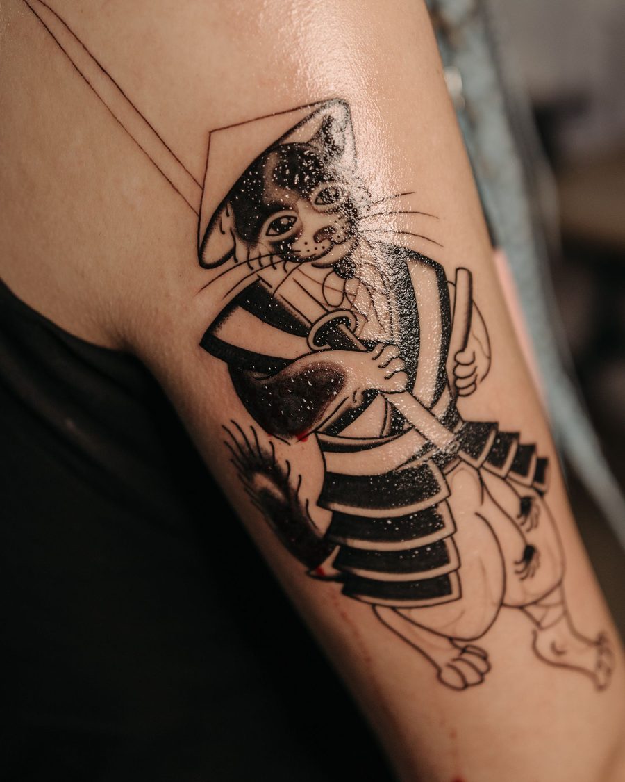 A bold blackwork samurai cat holding a sword on an upper arm