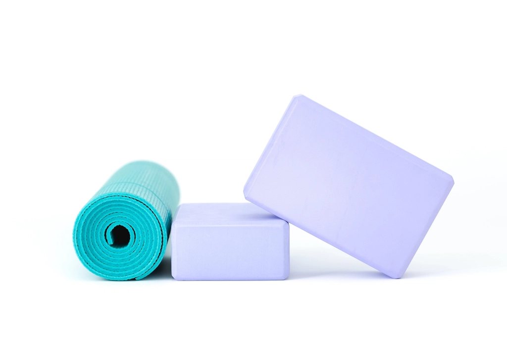 A rolled teal yoga mat beside two lilac foam blocks