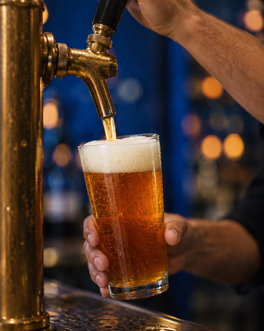 A bartender’s hand pouring amber beer from a brass tap into a pint glass